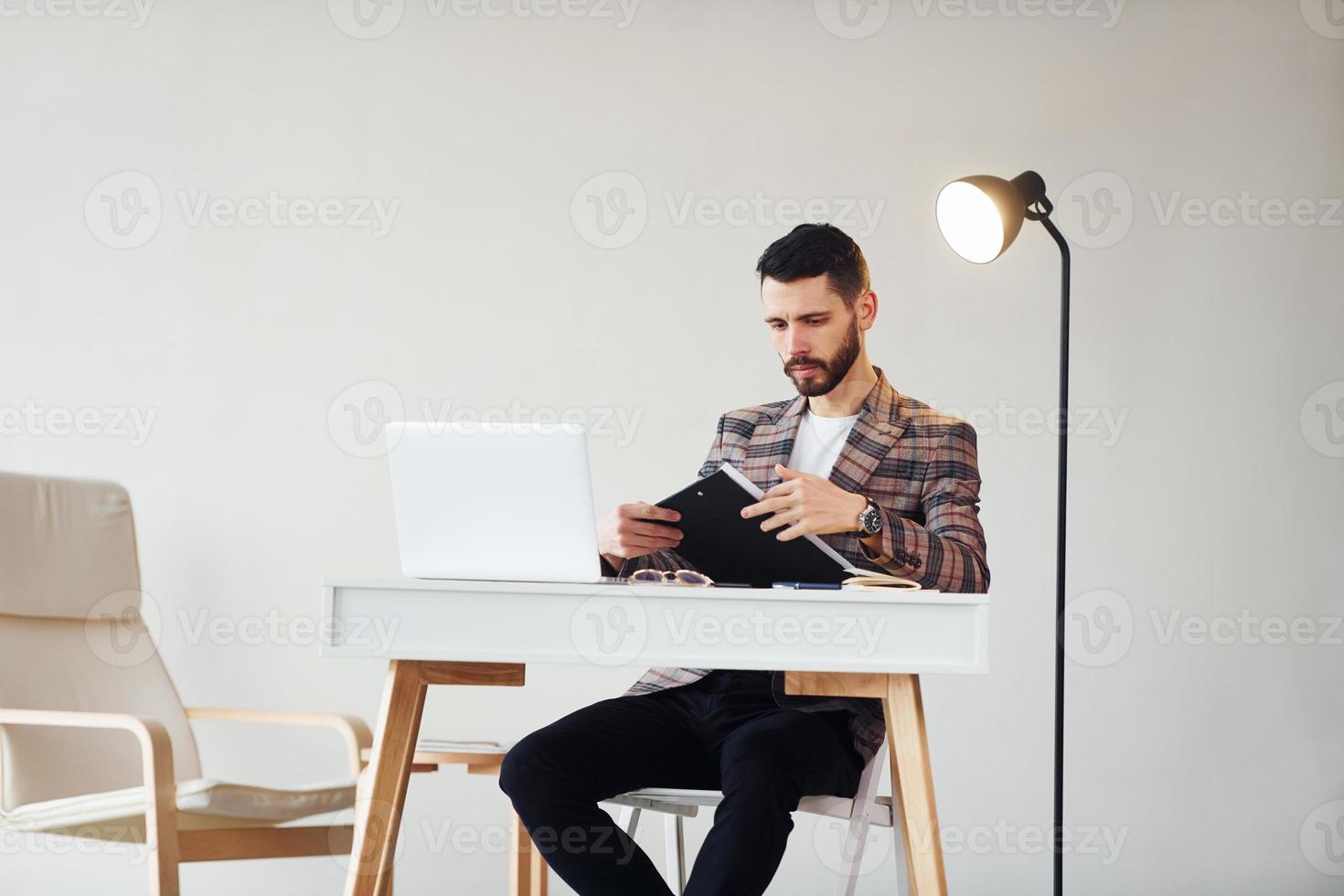 Uses laptop. Young stylish businessman in suit indoors. Conception of success photo