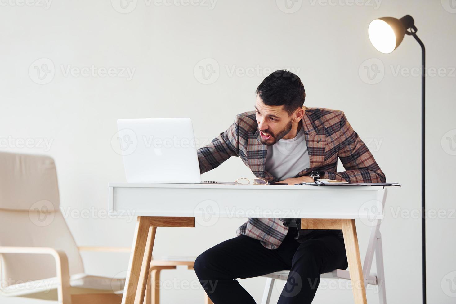 Uses laptop. Young stylish businessman in suit indoors. Conception of success photo