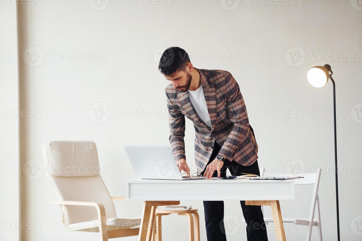 Works in the office. Young stylish businessman in suit indoors. Conception of success photo