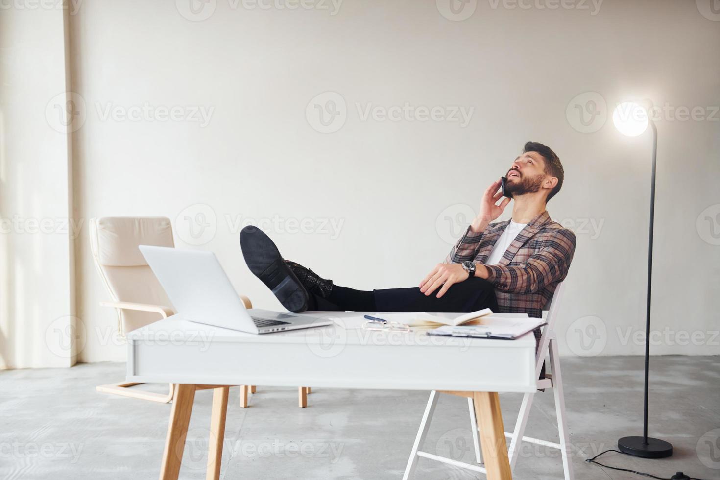 Have conversation by phone. Young stylish businessman in suit indoors. Conception of success photo