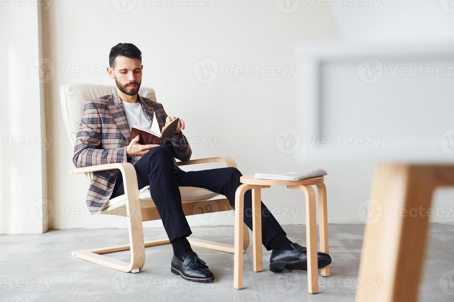 Reads book. Young stylish businessman in suit indoors. Conception of success photo