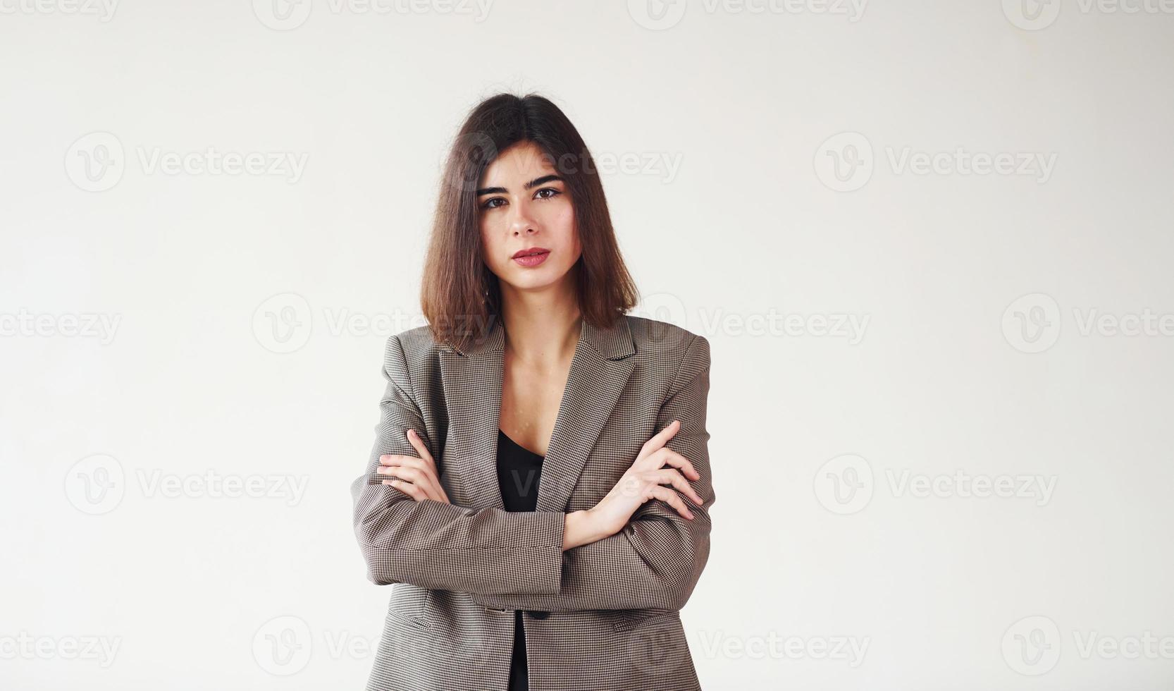 Young woman in formal clothes is standing against white background in the studio photo