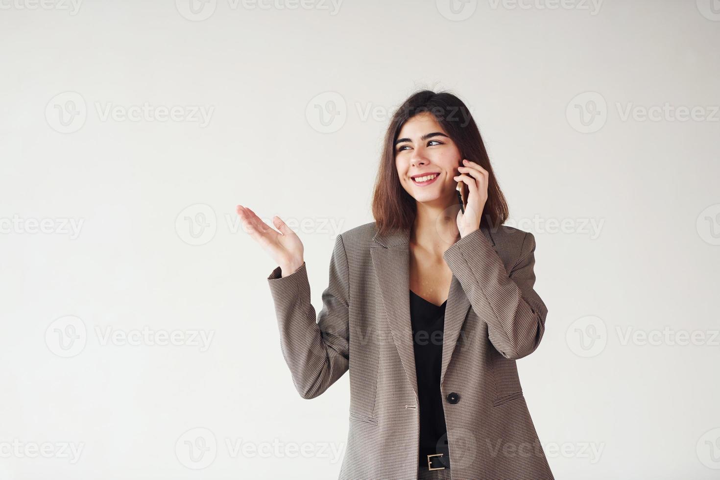 Young woman in formal clothes is standing against white background in the studio photo