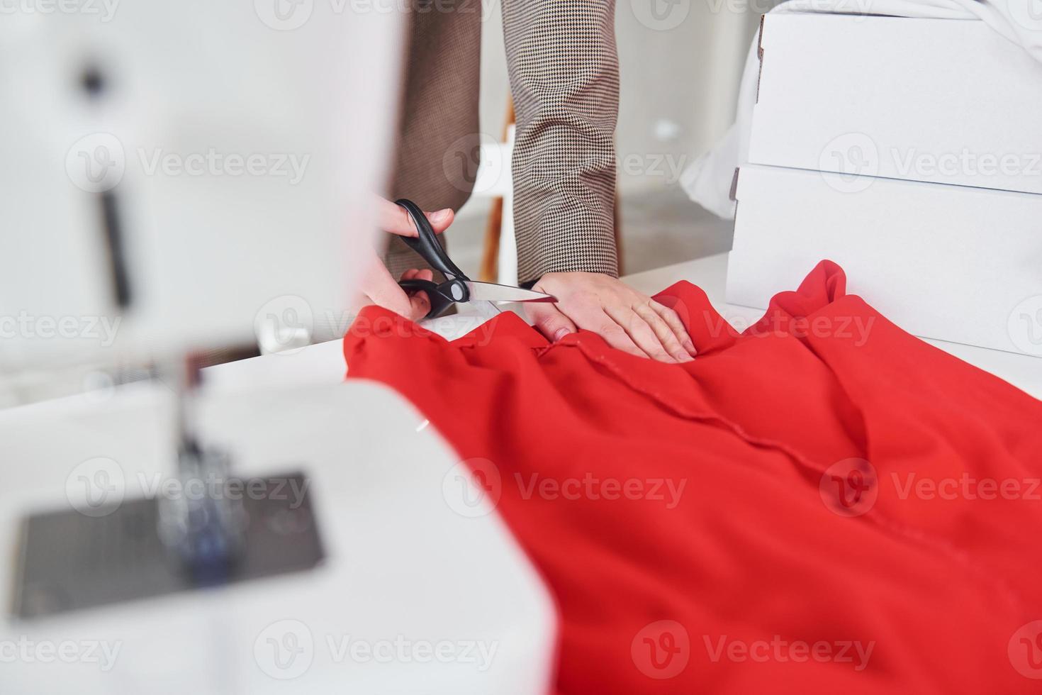 Close up view of seamstress that works with red cloth. Young woman in formal clothes is indoors photo