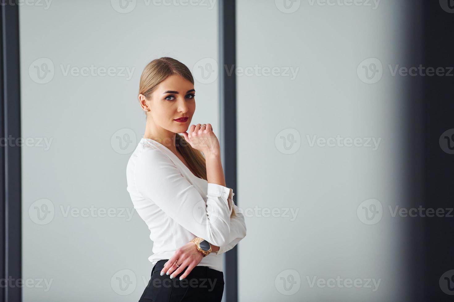 Standing against grey background. Young adult woman in formal clothes is indoors in the office photo