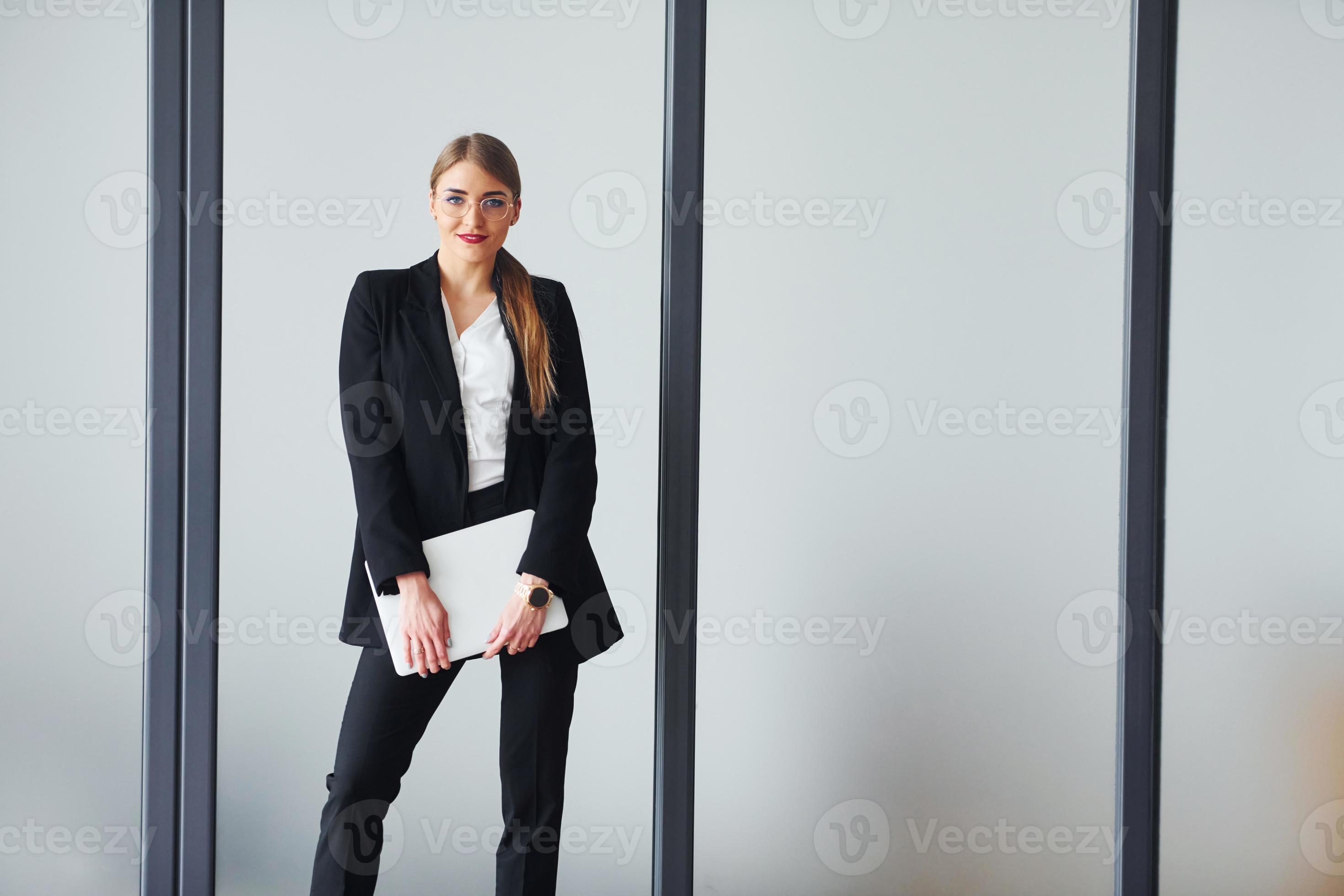 Young adult woman in formal clothes is indoors against grey