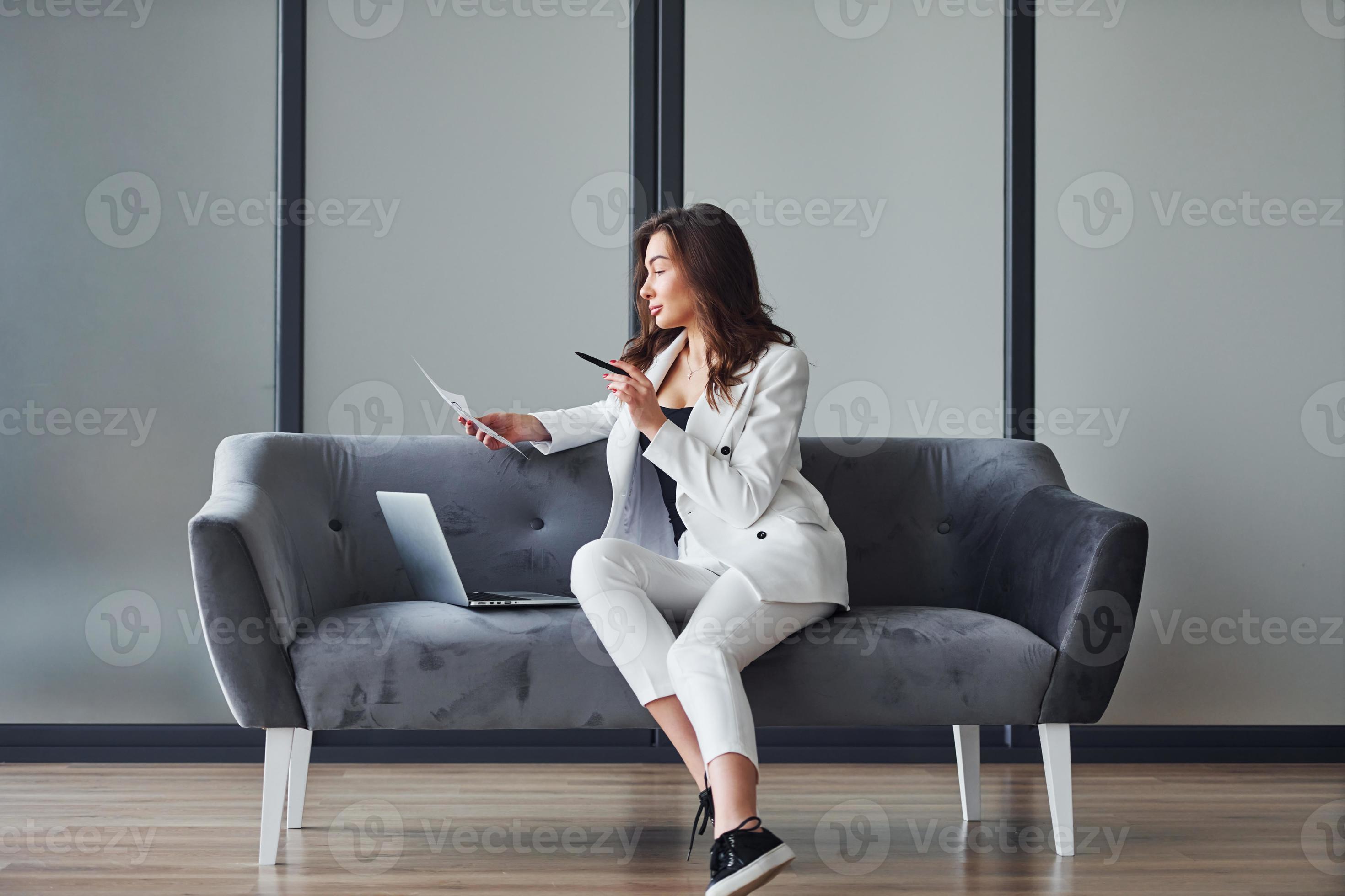 Young adult woman in formal clothes is indoors against grey