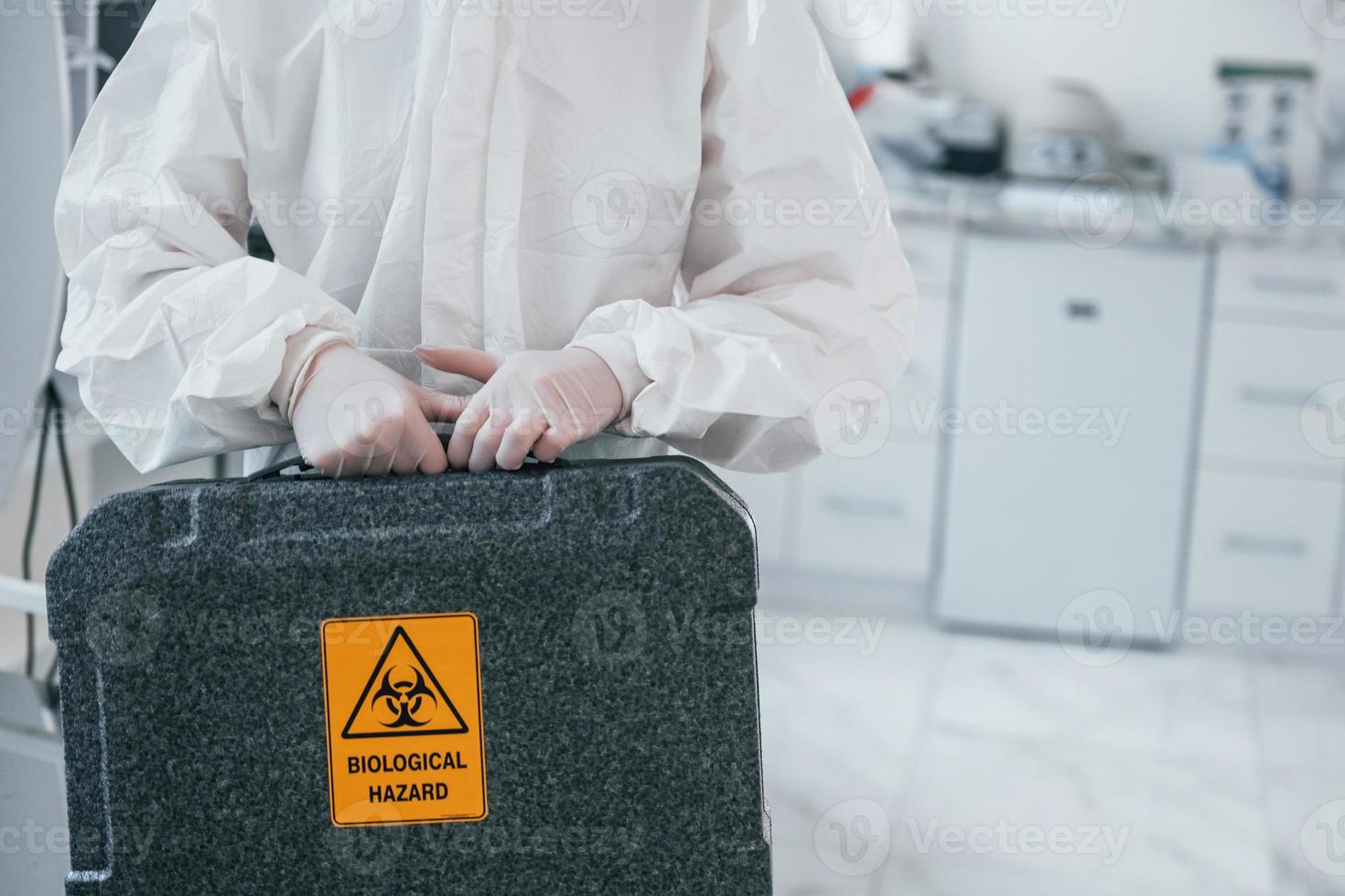 Holds case with biological hazard. Female medical worker in protective uniform works on COVID-19 vaccine photo