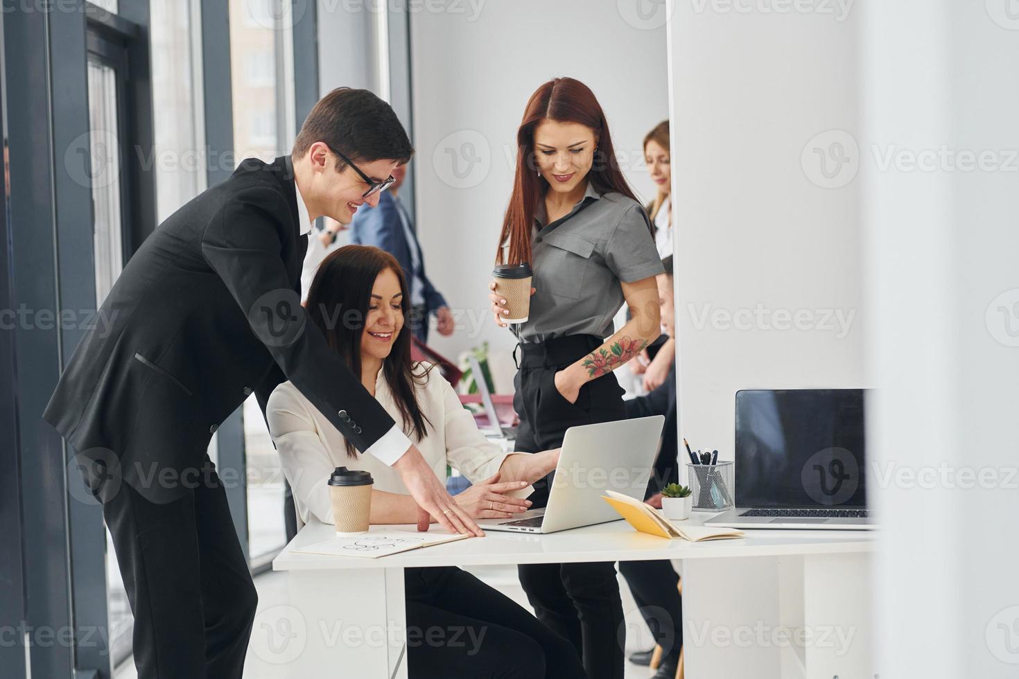 Works by using laptop. Group of people in official formal clothes that is indoors in the office photo