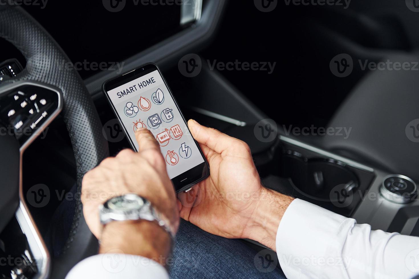 Sits in the car. Close up view of man's hand that holds phone with labels and icons. Conception of remote control photo