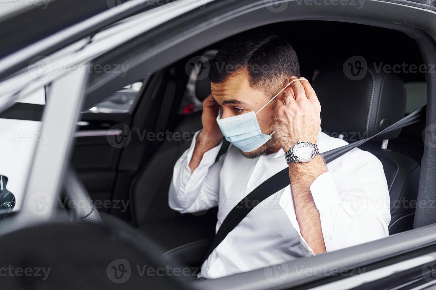 Young man in white shirt is sitting inside of a modern new automobile photo