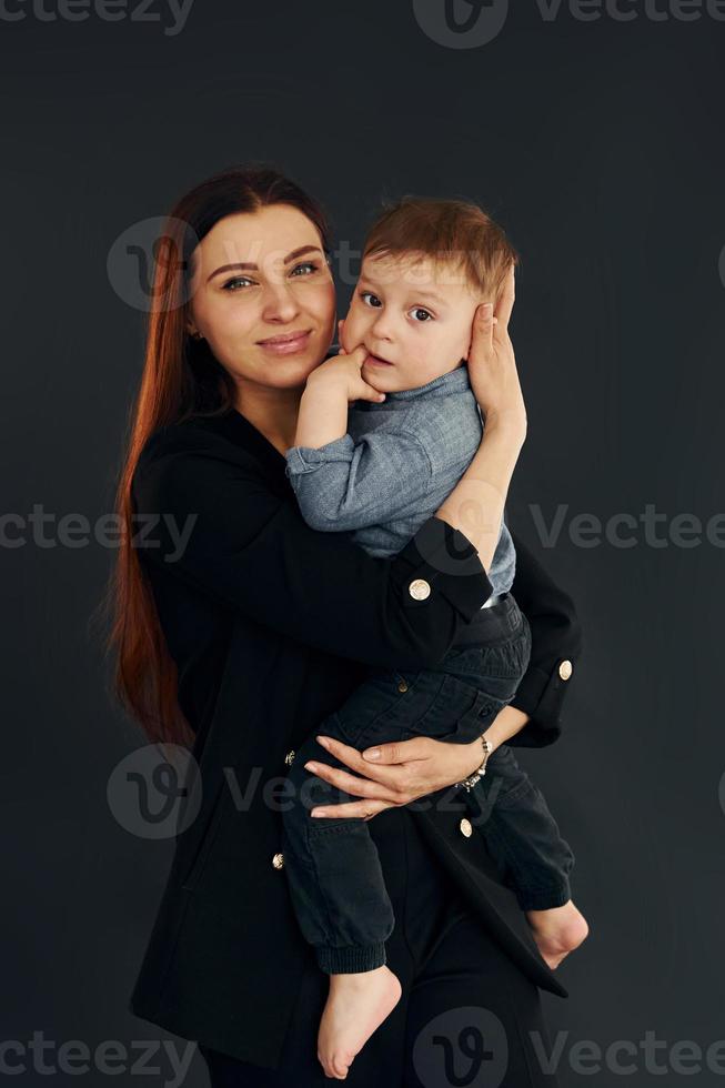 Mother in stylish black clothes is with her little son in the studio photo