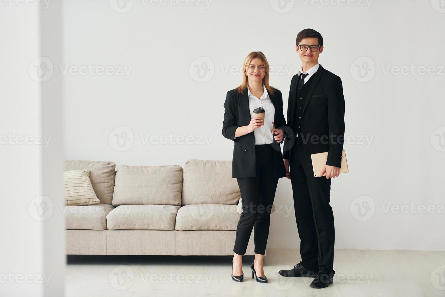 Young guys standing with woman indoors near sofa agaist white wall photo