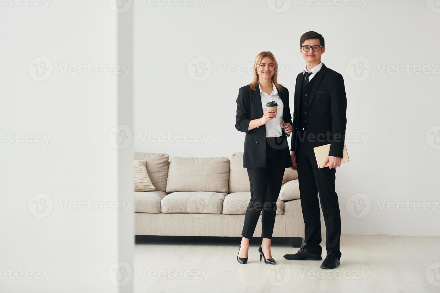 Young guys standing with woman indoors near sofa agaist white wall photo