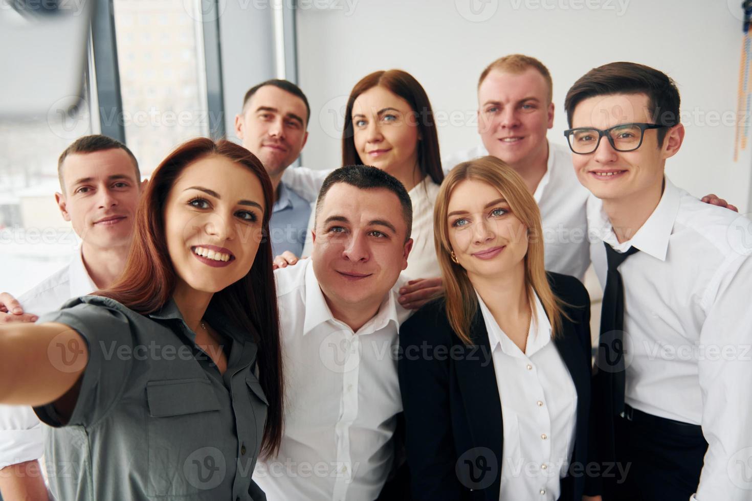 Makes selfie. Group of people in official formal clothes that is indoors in the office photo