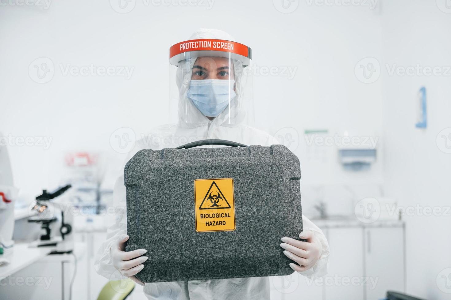 Holds case with biological hazard. Female medical worker in protective uniform works on COVID-19 vaccine photo
