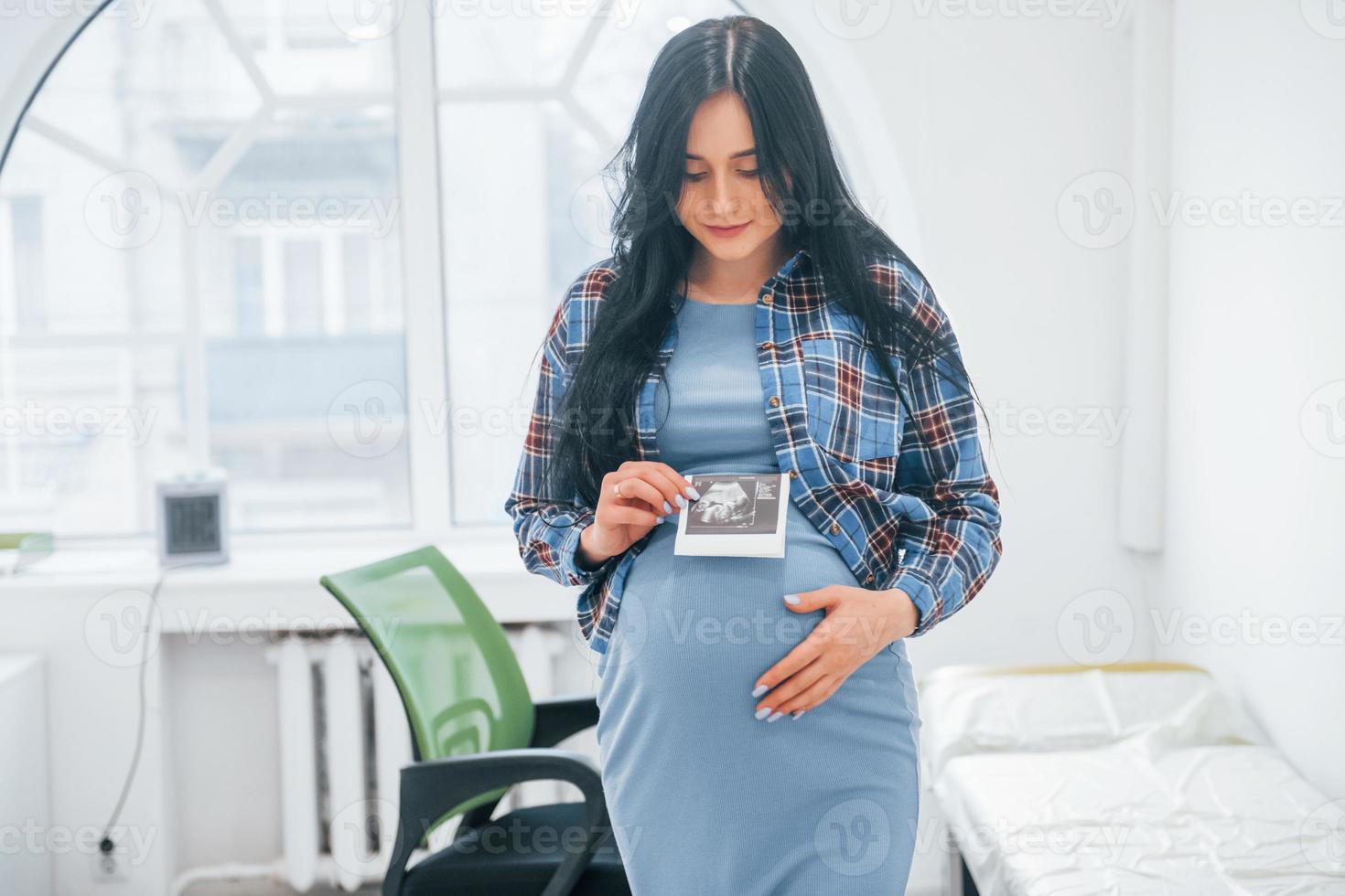 Holds results of ultrasonic scan. Pregnant woman is in the clinic in cabinet and have health check photo