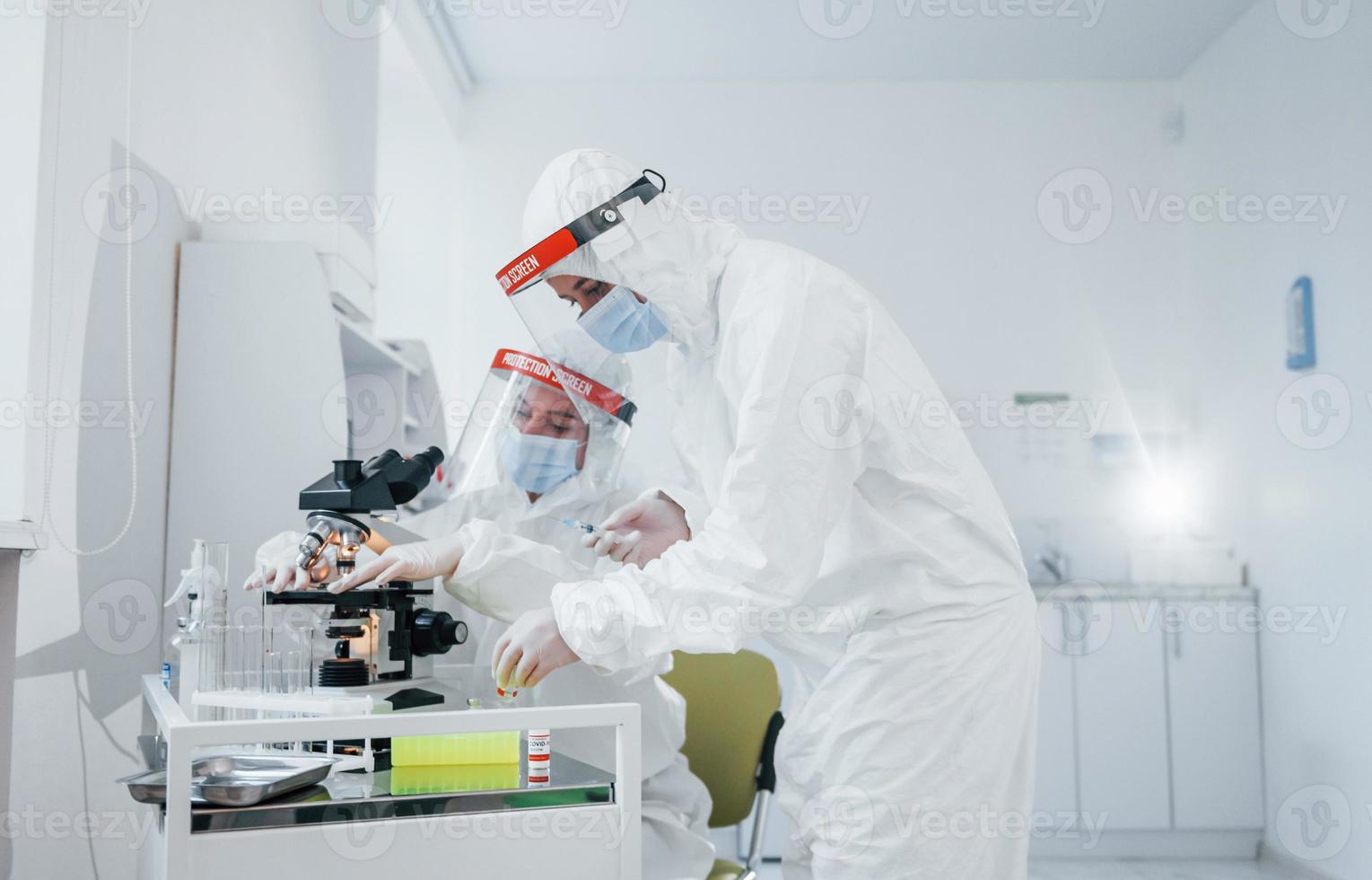 utilizando microscopio. trabajadoras médicas con uniforme protector trabajan en la vacuna covid-19 foto