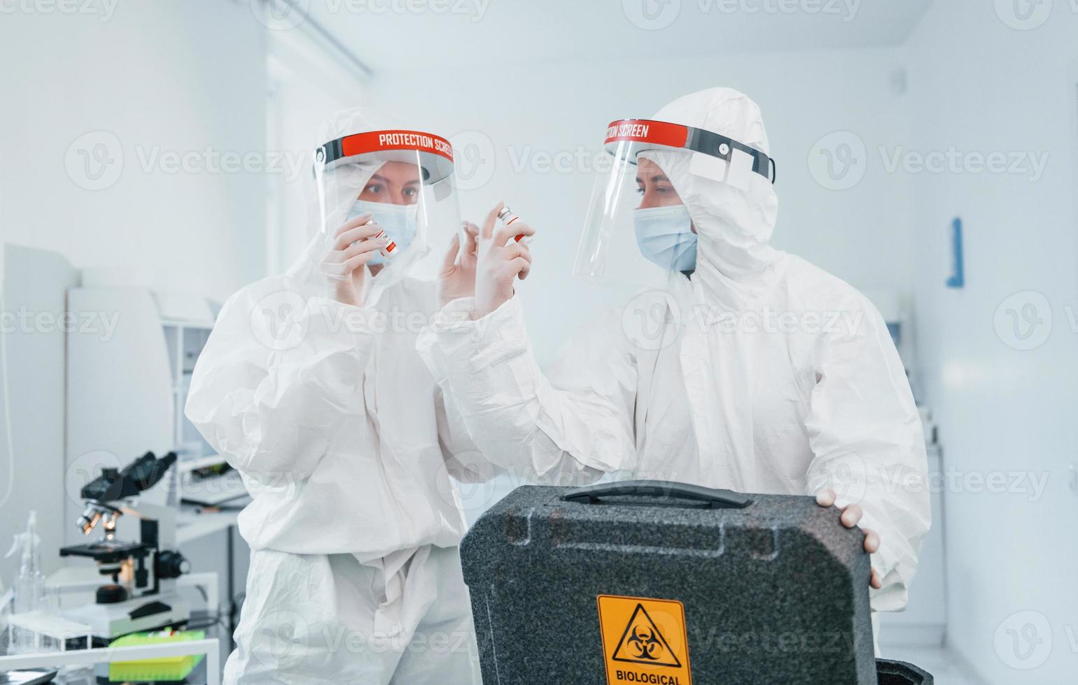 With biological hazard case. Female medical workers in protective uniform works on COVID-19 vaccine photo