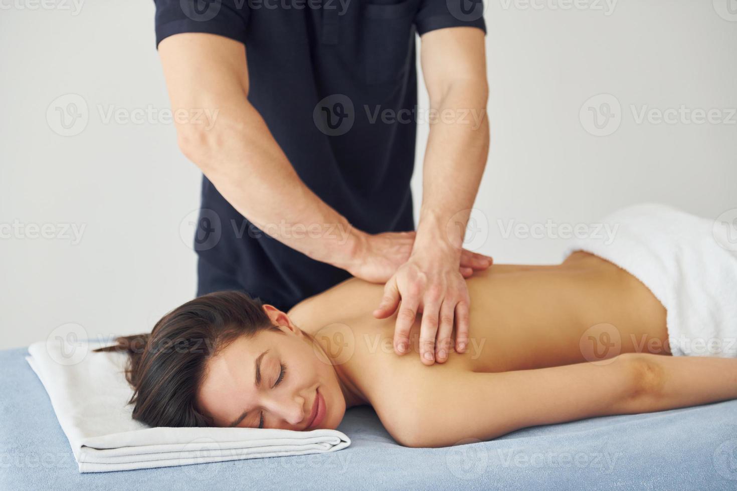 Young woman is lying down when man doing massage of her back at spa photo