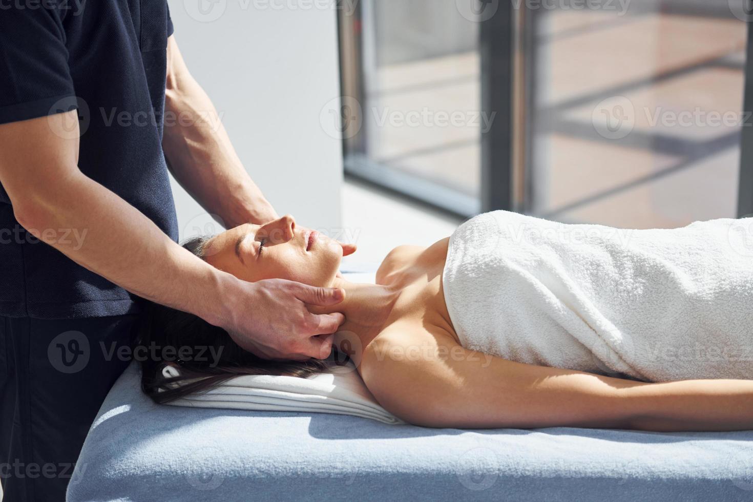 Room illuminated by sun beams. Young woman is lying down when man doing massage of her body at spa photo