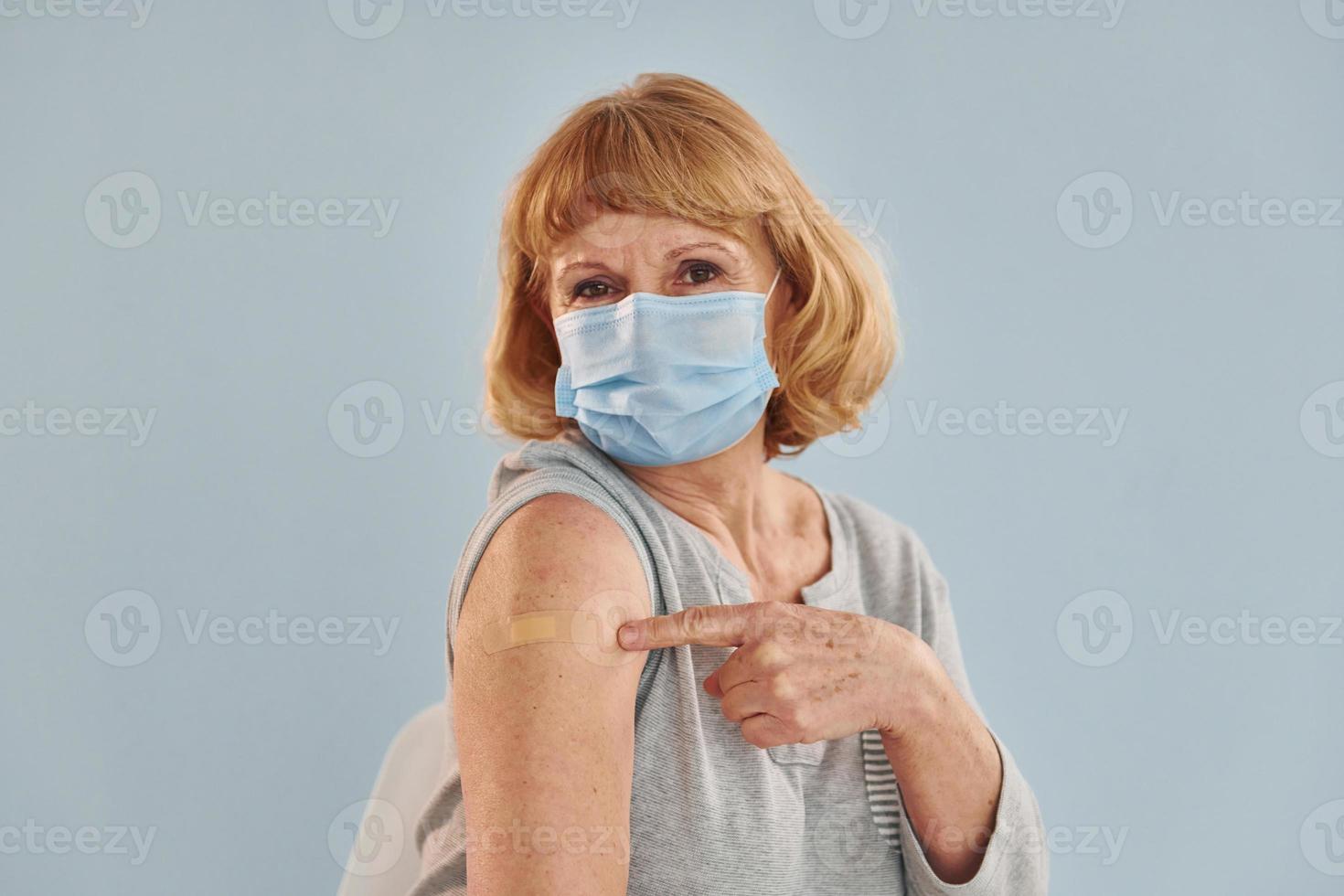Senior woman in mask is sits after vaccine injection indoors photo