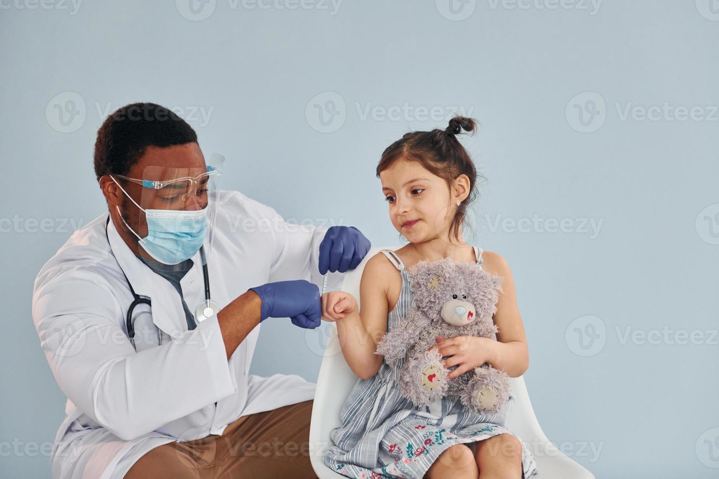 Young african american doctor giving injection to little girl at hospital photo