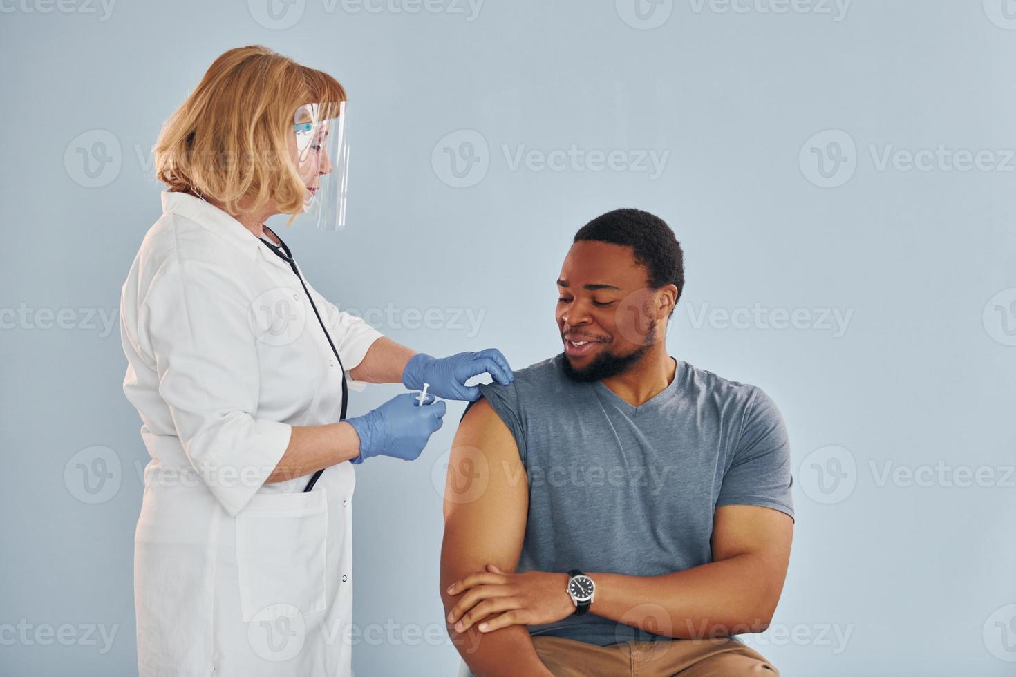 Senior doctor giving injection to young african american man at hospital photo