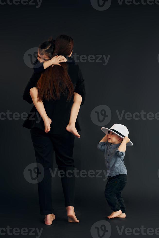 Woman in black stylish clothes is with her little son and daughter in the studio photo