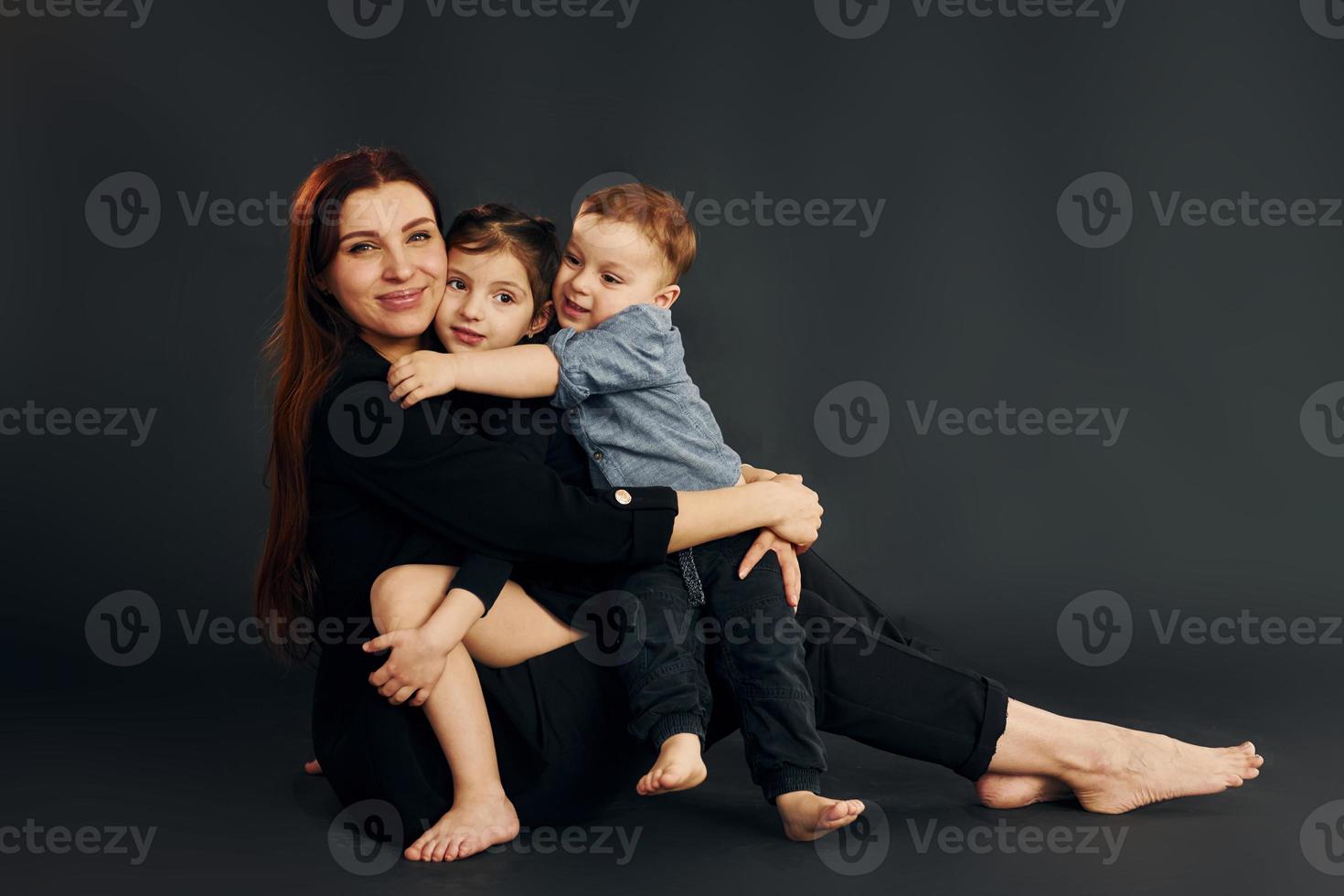 mujer vestida de negro con estilo está con su pequeño hijo y su hija en el estudio foto