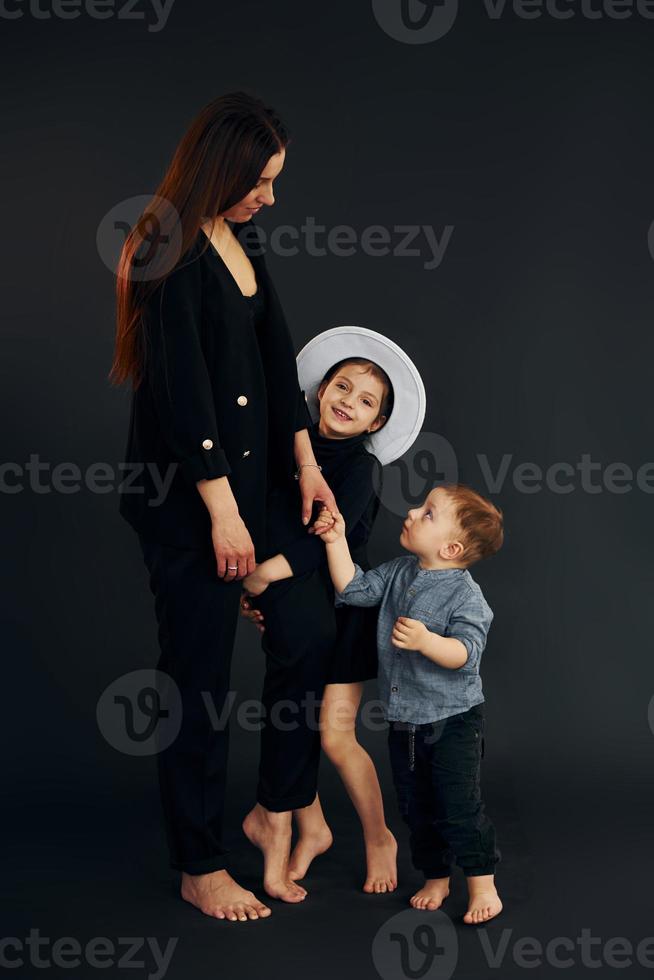 Woman in black stylish clothes is with her little son and daughter in the studio photo