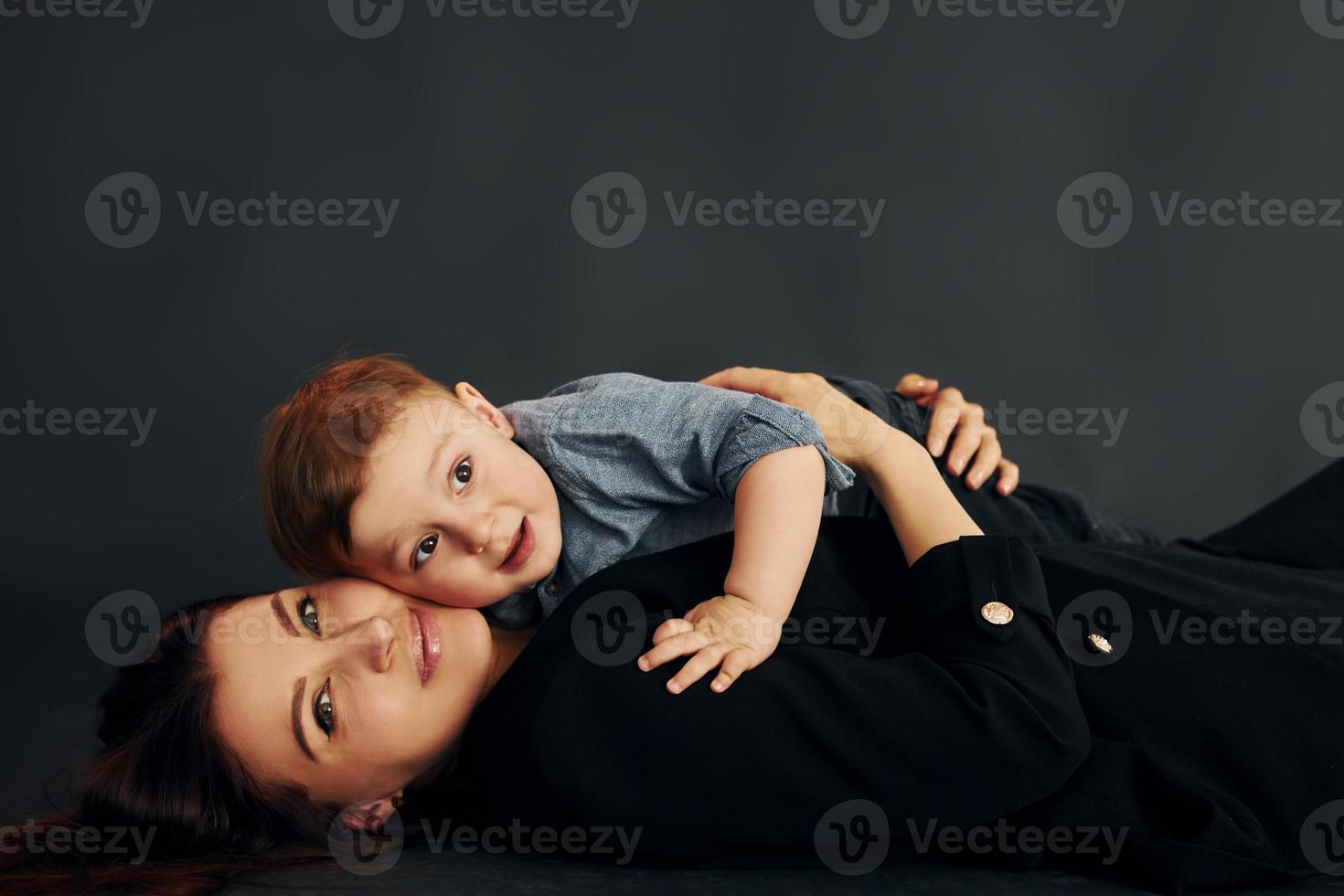 madre con ropa negra elegante está con su pequeño hijo en el estudio foto