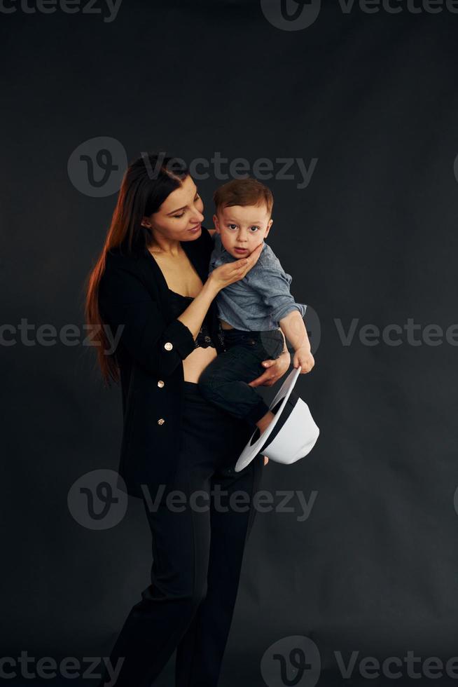 madre con ropa negra elegante está con su pequeño hijo en el estudio foto