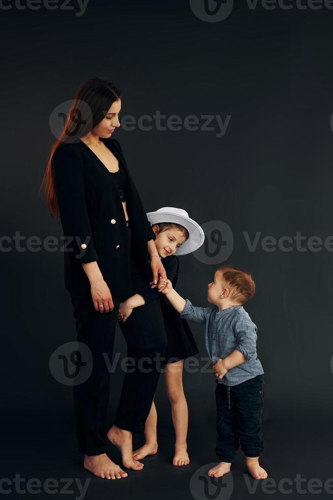 Woman in black stylish clothes is with her little son and daughter in the studio photo