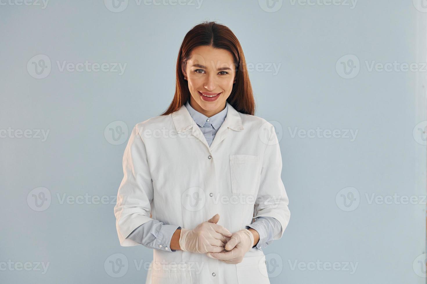 una joven doctora con bata blanca está de pie en el interior contra el fondo azul foto