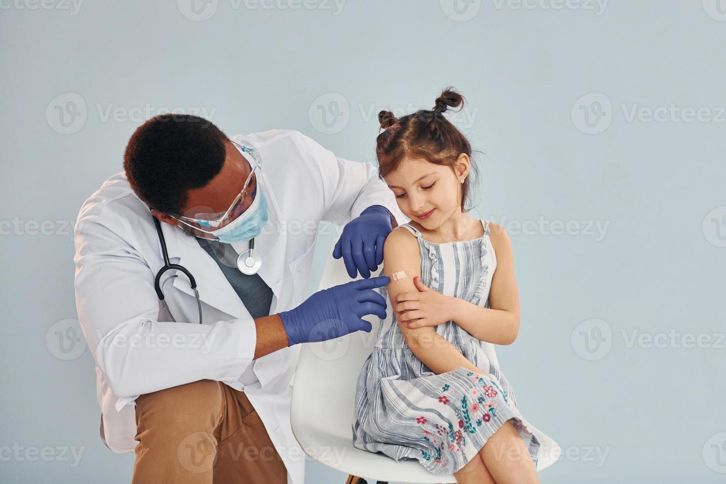 Young african american doctor giving injection to little girl at hospital photo