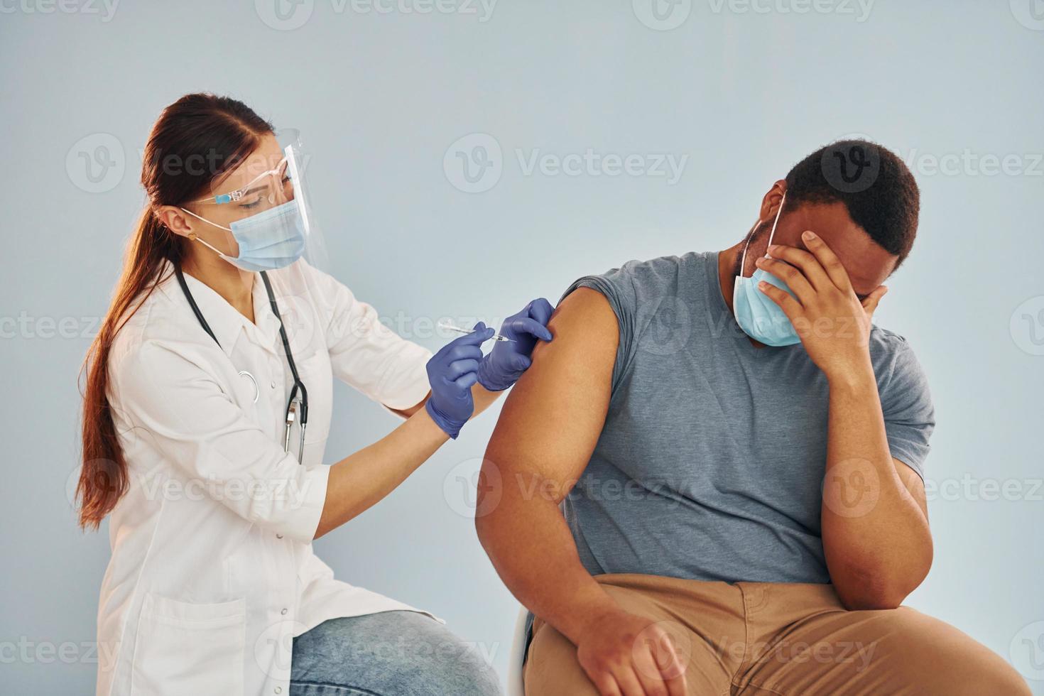 Female doctor giving injection to african american man at hospital photo