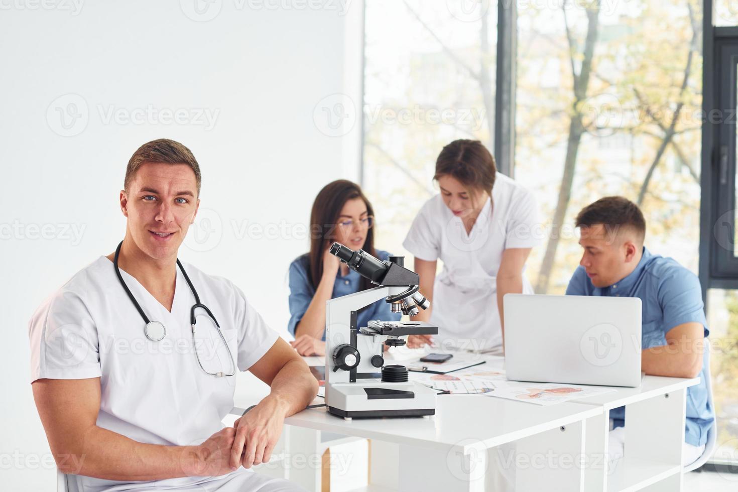 Using microscope. Group of young doctors is working together in the modern office photo