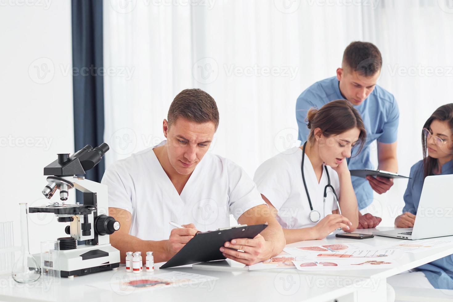 utilizando microscopio. grupo de médicos jóvenes está trabajando juntos en la oficina moderna foto