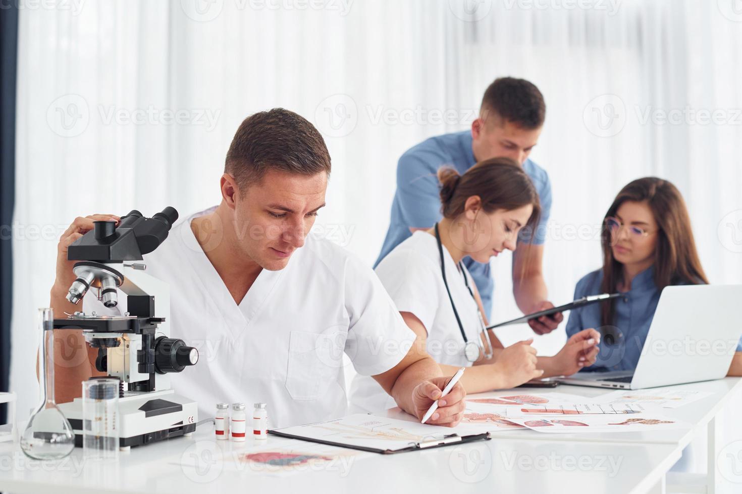 hombre con microscopio. grupo de médicos jóvenes está trabajando juntos en la oficina moderna foto