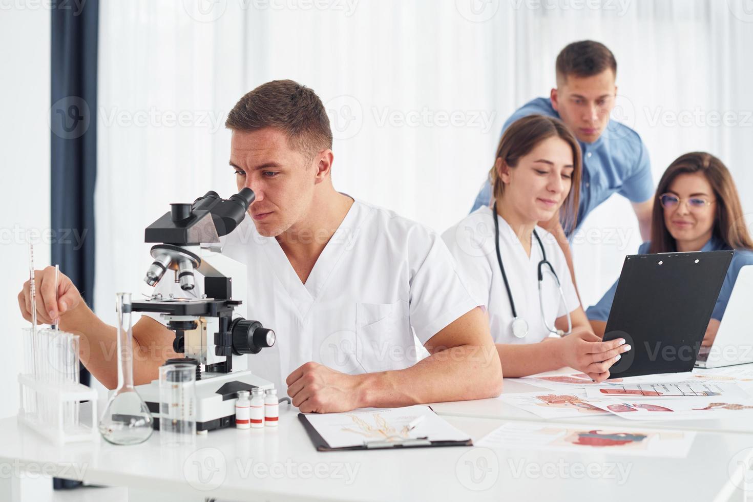 hombre con microscopio. grupo de médicos jóvenes está trabajando juntos en la oficina moderna foto