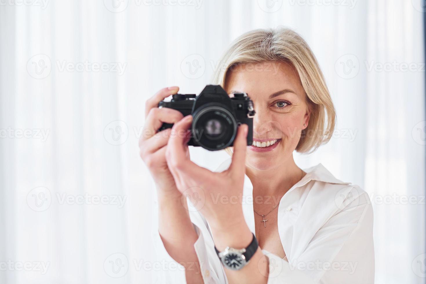 mujer de mediana edad con ropa elegante está en casa. fotógrafo con cámara foto