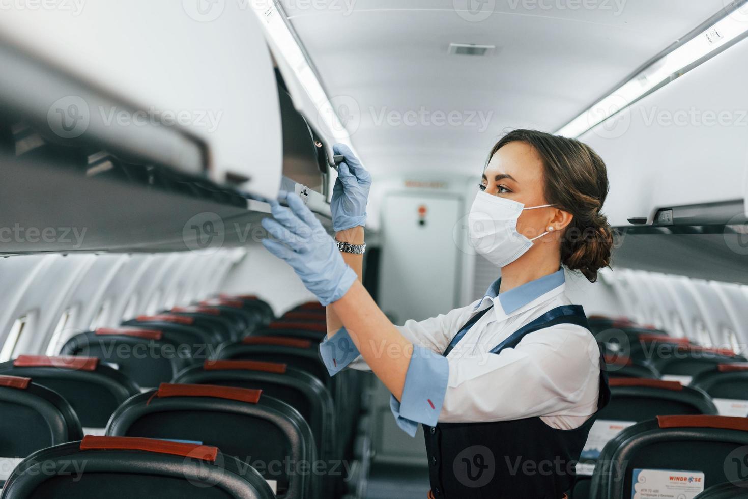 In protective gloves and mask. Young stewardess on the work in the passanger airplane photo