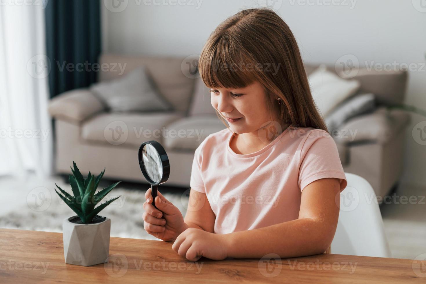 Little girl is sitting by the table with magnifying glass photo