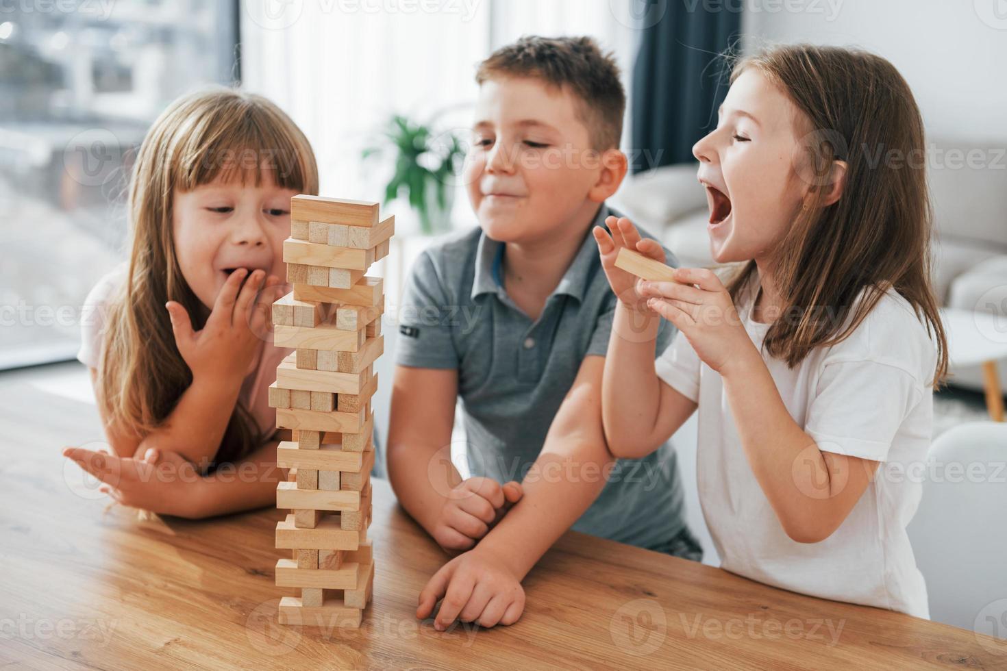 Focused on the jumbling tower game. Kids having fun in the domestic room at daytime together photo