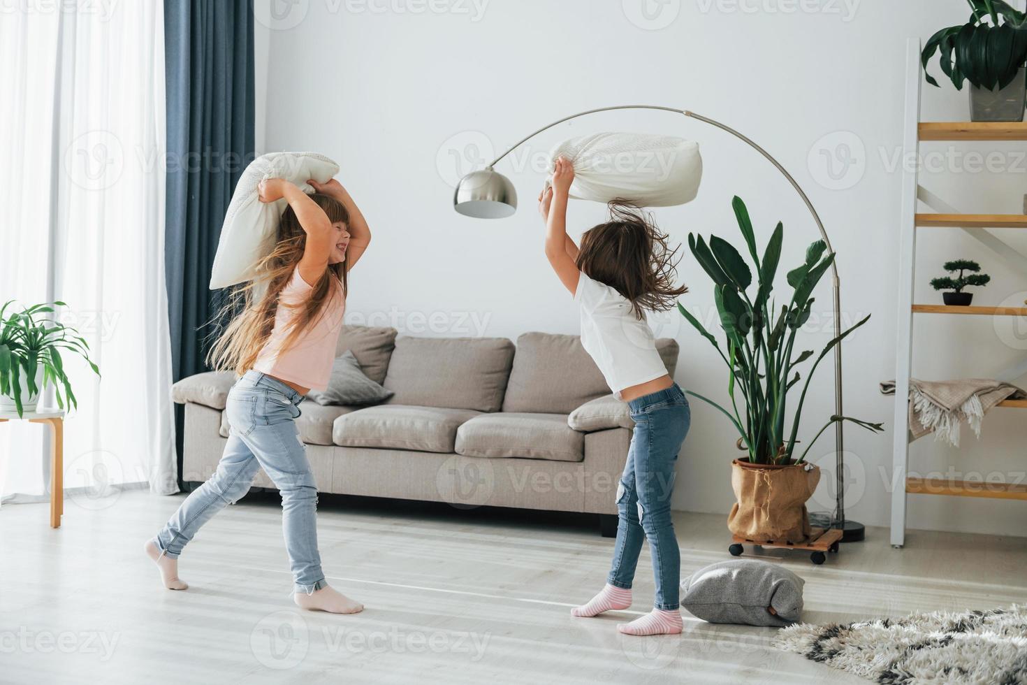 las chicas están jugando al juego de pelea de almohadas. niños divirtiéndose juntos en la sala doméstica durante el día foto