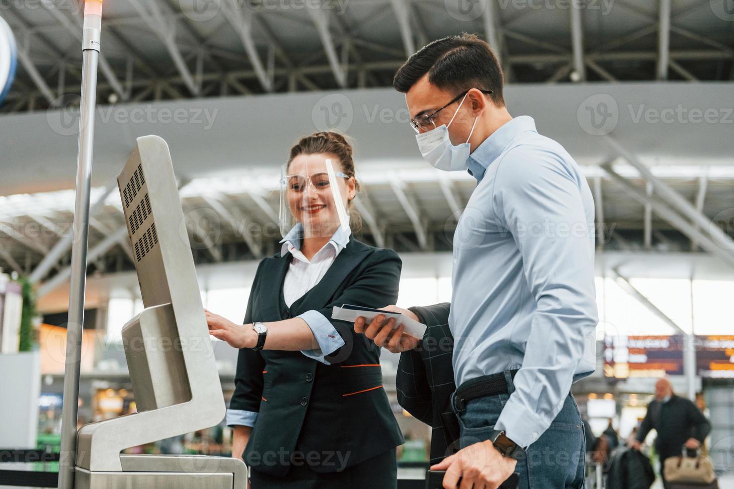 Employee helping using terminal. Young businessman in formal clothes is in the airport at daytime photo