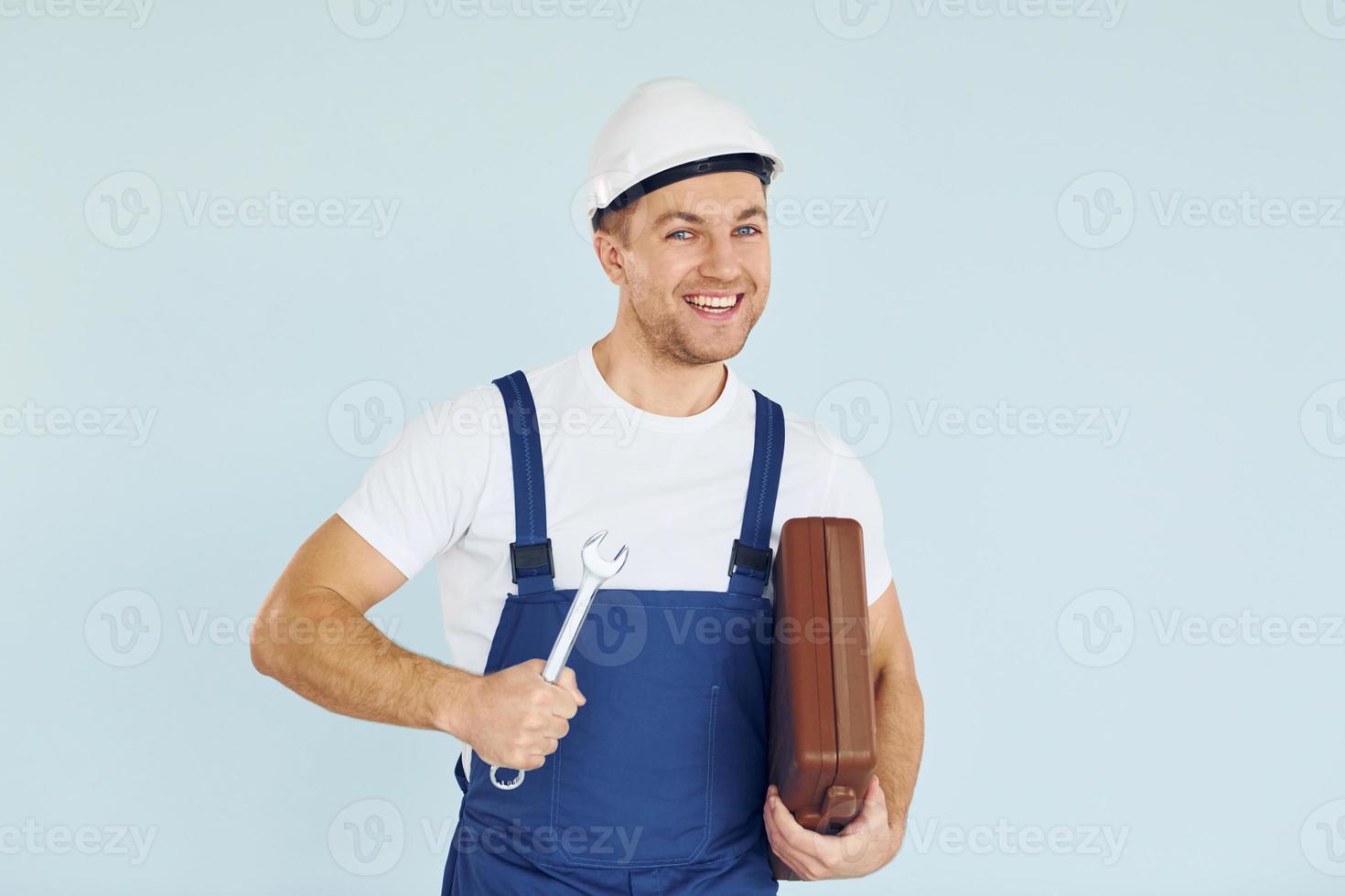 Holding brown case. Worker in uniform and hard hat standing in the studio with equipment photo