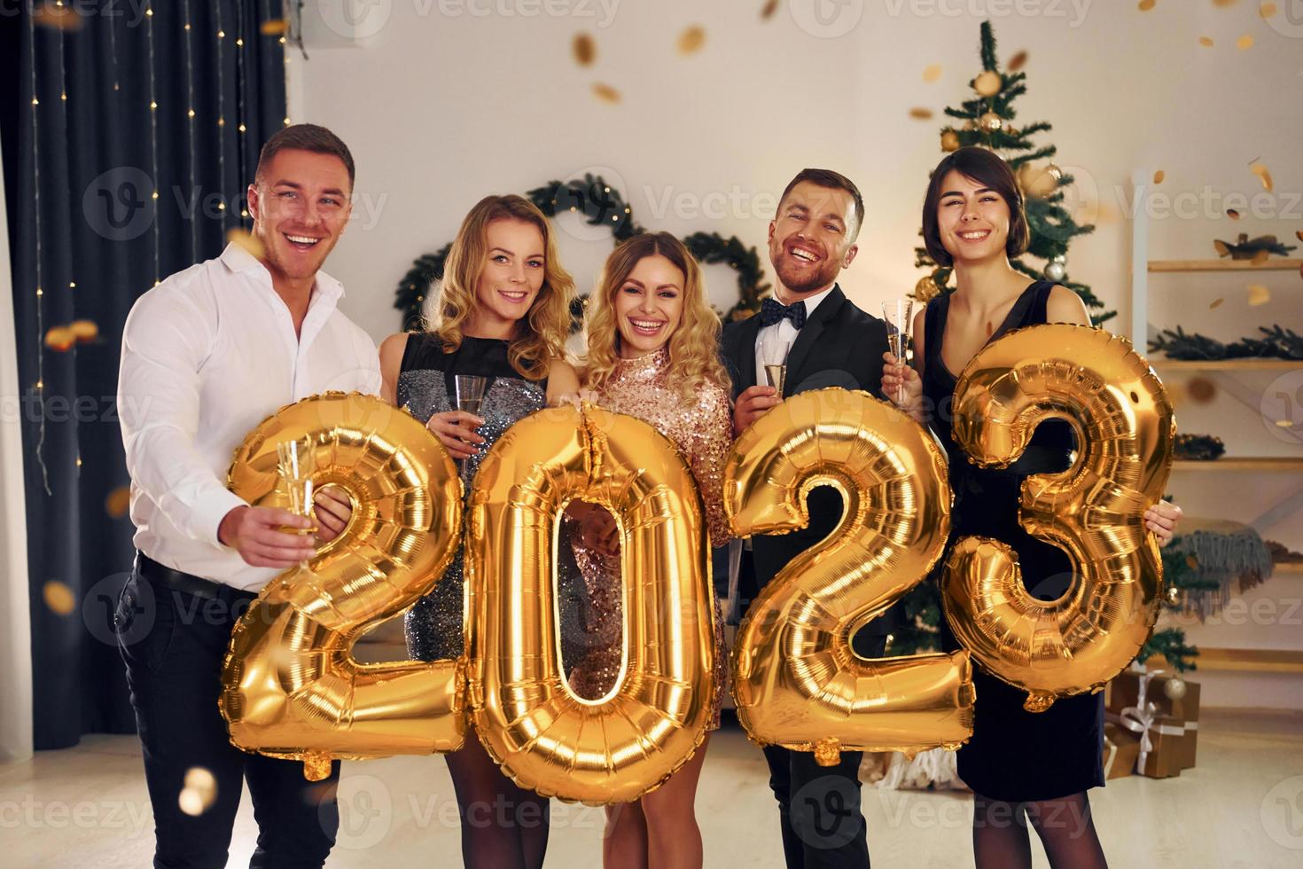 sosteniendo globos con el número 2023. grupo de personas tienen una fiesta de año nuevo en el interior juntos foto