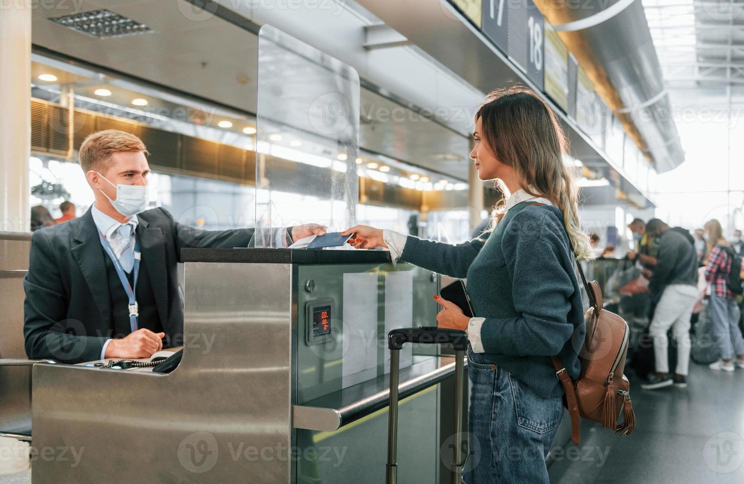 Standing by the table with employee. Young female tourist is in the airport at daytime photo